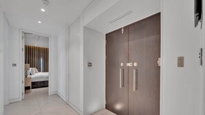 Ein moderner Hotelkorridor mit einer Doppeltür, einem Bett mit Kopfteil und einem hell gefliesten Boden.
