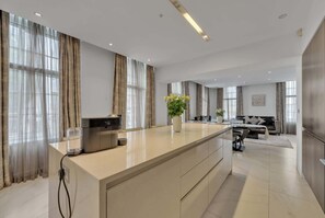 Une cuisine moderne dotée d’un îlot central, de grandes fenêtres avec des rideaux et d’un coin repas comprenant un canapé et une table.