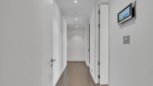A modern hallway with white walls, a wooden floor, and a mounted digital display on the right wall. - Stylish Apartment with AC in Baker St (Greater London)
