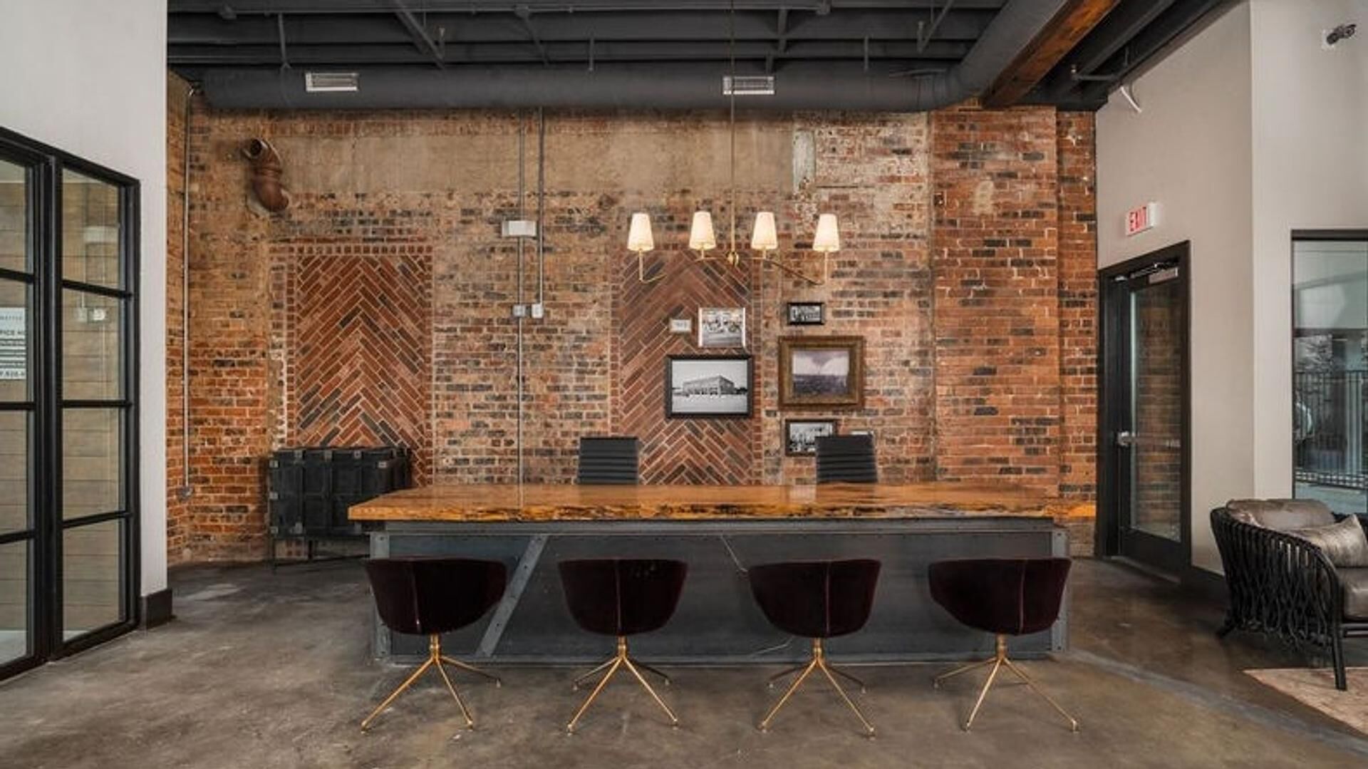 A modern bar area with a brick wall, pendant lighting, and a bar counter with three black chairs.