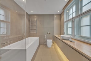 A modern bathroom with a bathtub, toilet, and sink, featuring a large window and a glass shower enclosure. - Beautiful apartment with lift in Baker St (Greater London)