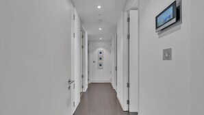 A modern hallway with white walls, a wooden floor, and a mounted digital display on the right wall. - Beautiful apartment with lift in Baker St (Greater London)