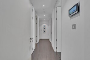 A modern hallway with white walls, wooden flooring, and a mounted television screen. - Beautiful apartment with lift in Baker St (Greater London)