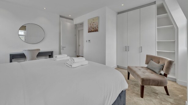 Un dormitorio con una cama grande, una mesita de noche, una silla, un armario y un espejo.