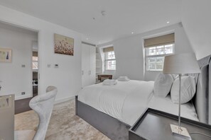 A modern bedroom with a bed, bedside table, lamp, and a chair.