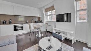 Una cocina moderna con armarios blancos, un comedor con una mesa redonda y un televisor montado en la pared.