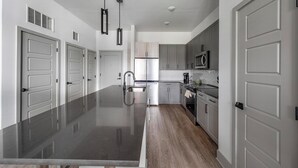 A modern kitchen with a central island, stainless steel appliances, and grey cabinetry. - Landing | Stylish 2BD, Pool, Gym (Nashville)