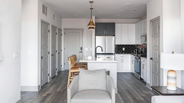 Een moderne keuken met witte kasten, een centraal eiland en een zithoek met een grijze bank en houten stoelen.