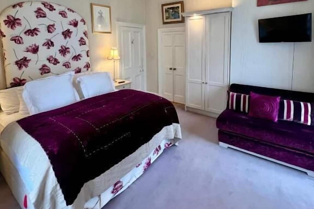 A bedroom with a bed, a sofa, a wardrobe, and a television.
