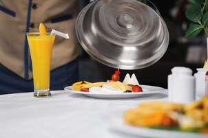 A breakfast setting with a glass of orange juice, a plate of fruit, and a metal container.