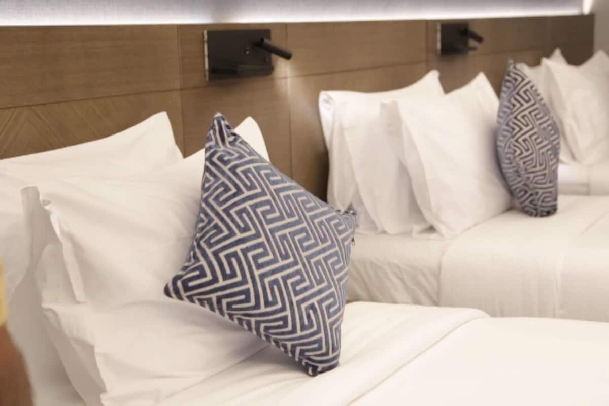 Ein Hotelzimmer mit zwei Betten, jeweils mit weißer Bettwäsche und gemusterten Kissen.