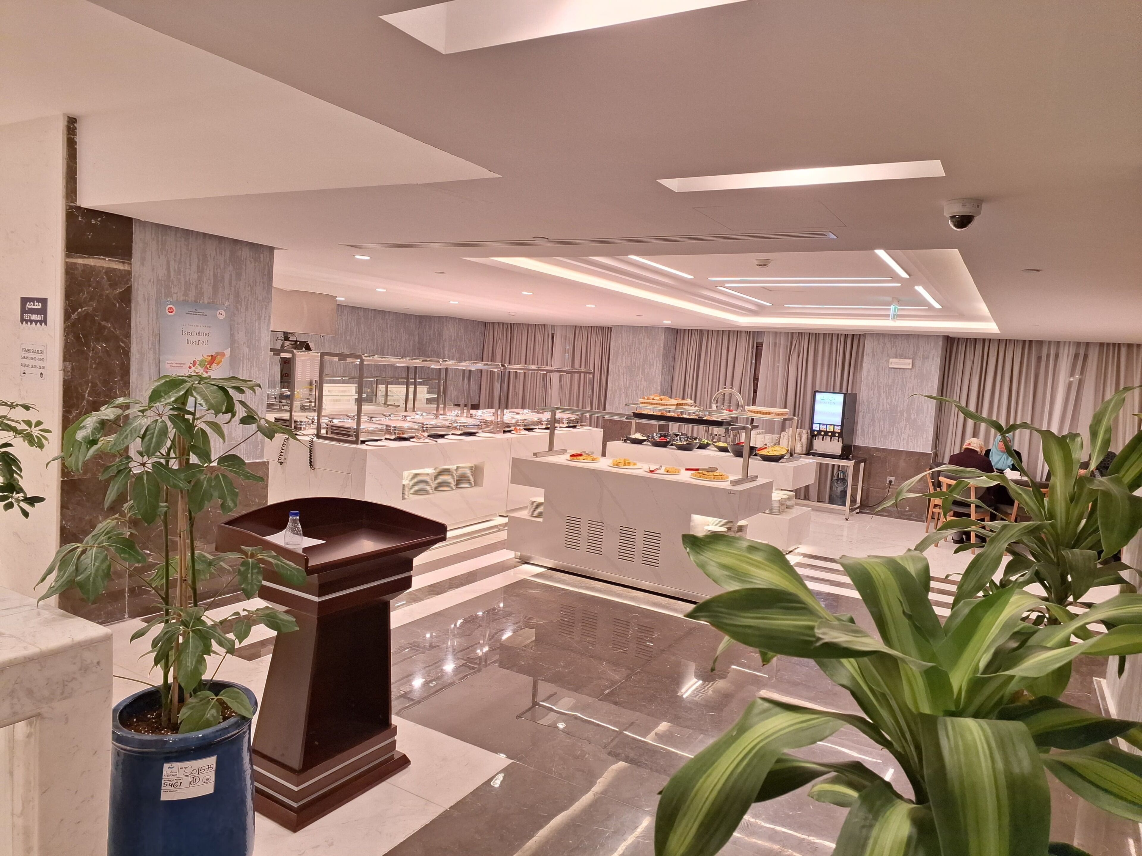 Un moderno vestíbulo de hotel con zona de buffet, suelo de mármol y plantas en macetas.