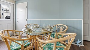 A dining area with a glass-top table, wicker chairs, and a light blue wall. - Charming 2nd Floor Bayside Condo, Steps to Pool & Beach! (Ocean City)