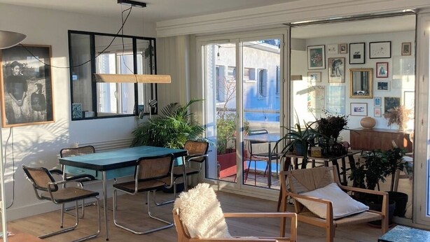 A spacious living area with a dining table, chairs, a sofa, and a coffee table. There are potted plants and a large window providing a view outside. - Buttes Chaumont top floor loft: unobstructed view of Paris! (Paris)