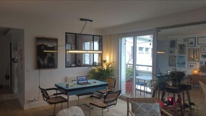 A modern living room with a blue dining table, two chairs, a laptop, and a potted plant. There is a large window with a view of the outside. - Buttes Chaumont top floor loft: unobstructed view of Paris! (Paris)