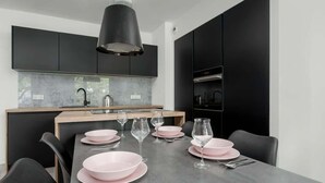 A modern kitchen with dark cabinets, a marble countertop, and a dining table set with pink plates and wine glasses. - Stylish Apartment with 2 Bedrooms | Balcony and Parking (Wroclaw)