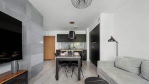 A modern living room with a flat-screen TV, a grey sofa, a dining area with a table and chairs, and a kitchen in the background. - Stylish Apartment with 2 Bedrooms | Balcony and Parking (Wroclaw)