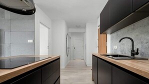 A narrow kitchen with black cabinets, a wooden countertop, and a modern faucet. - Stylish Apartment with 2 Bedrooms | Balcony and Parking (Wroclaw)