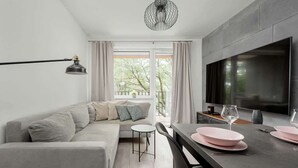 A modern living room with a sofa, a dining table, a TV, and a pendant light. - Stylish Apartment with 2 Bedrooms | Balcony and Parking (Wroclaw)