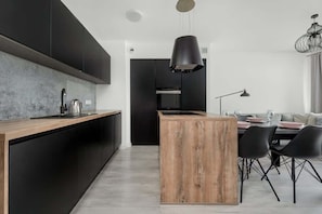 Cozinha moderna com armários escuros, uma ilha de madeira e uma área de jantar com cadeiras pretas.