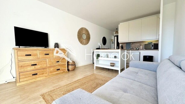 Un soggiorno moderno con un divano grigio, un mobile TV in legno e un angolo cottura sullo sfondo.