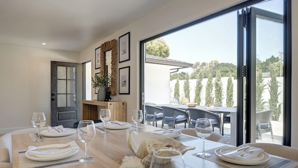 A dining area with a wooden table set for four, a view of the outdoors through large windows, and a door leading to another room. - 3944 Seaside Bash - Central Carmel Location (Carmel)