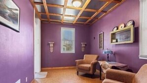 Una habitación con paredes moradas, techo de madera, dos sillas, una mesa y una ventana.