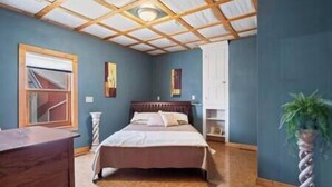 Un dormitorio con techo de madera, una cama, un aparador y una planta en maceta.
