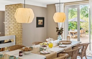 A dining area with a brick wall, two hanging pendant lights, a table set with plates, glasses, and a pitcher of orange juice.