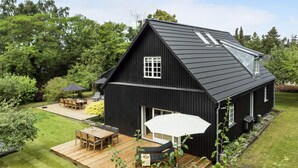 A black house with a sloped roof, a large window, and a deck with outdoor furniture.