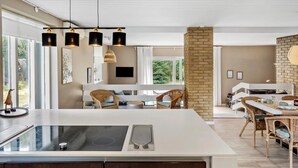 A modern kitchen with a large island, built-in appliances, and a dining area with wicker furniture.