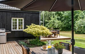 A wooden deck with a grill, a table with a pitcher of orange juice, and a potted plant.