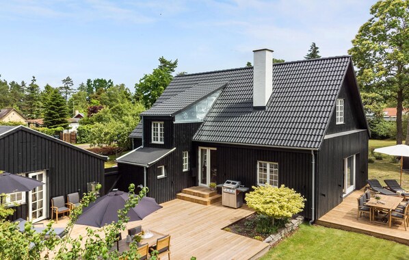 A two-story house with a dark exterior, a chimney, and a deck with outdoor furniture.