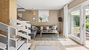 A modern living room with a staircase, a sofa set, a coffee table, and a large sliding glass door leading to an outdoor area.