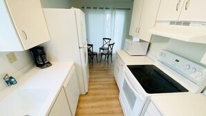 Una kitchenette compacta con electrodomésticos blancos, un pequeño comedor con dos sillas y piso de madera.