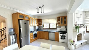 A modern kitchen with wooden cabinets, stainless steel appliances, and a dining area with a white table and chairs.