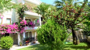A two-story building with balconies, surrounded by lush greenery and flowering plants.