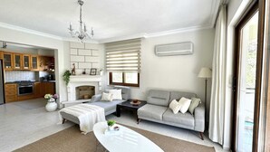 A spacious living room with a fireplace, a sofa, a coffee table, and a kitchen in the background.
