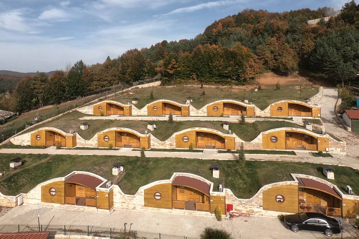 A row of wooden cabins with pitched roofs, arranged in a terraced layout on a hillside.