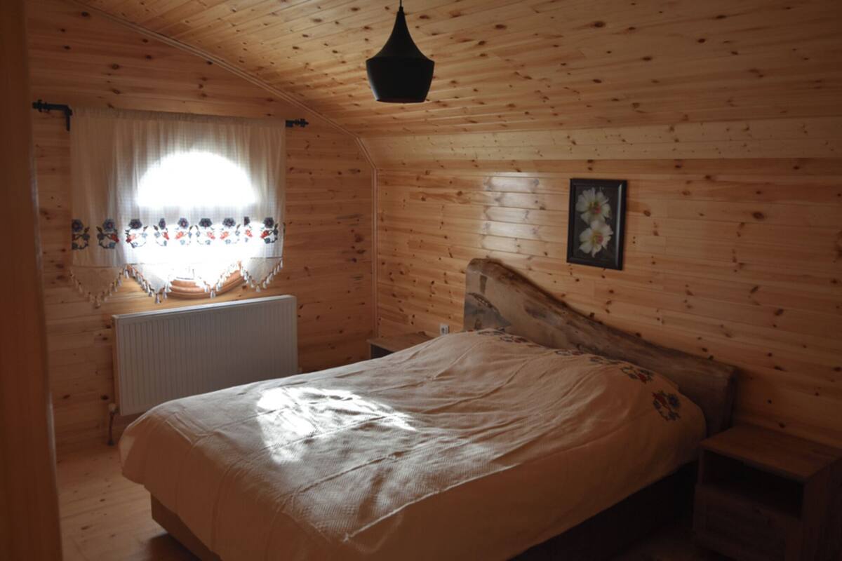 A wooden cabin bedroom with a bed, a window with curtains, and a hanging light fixture.