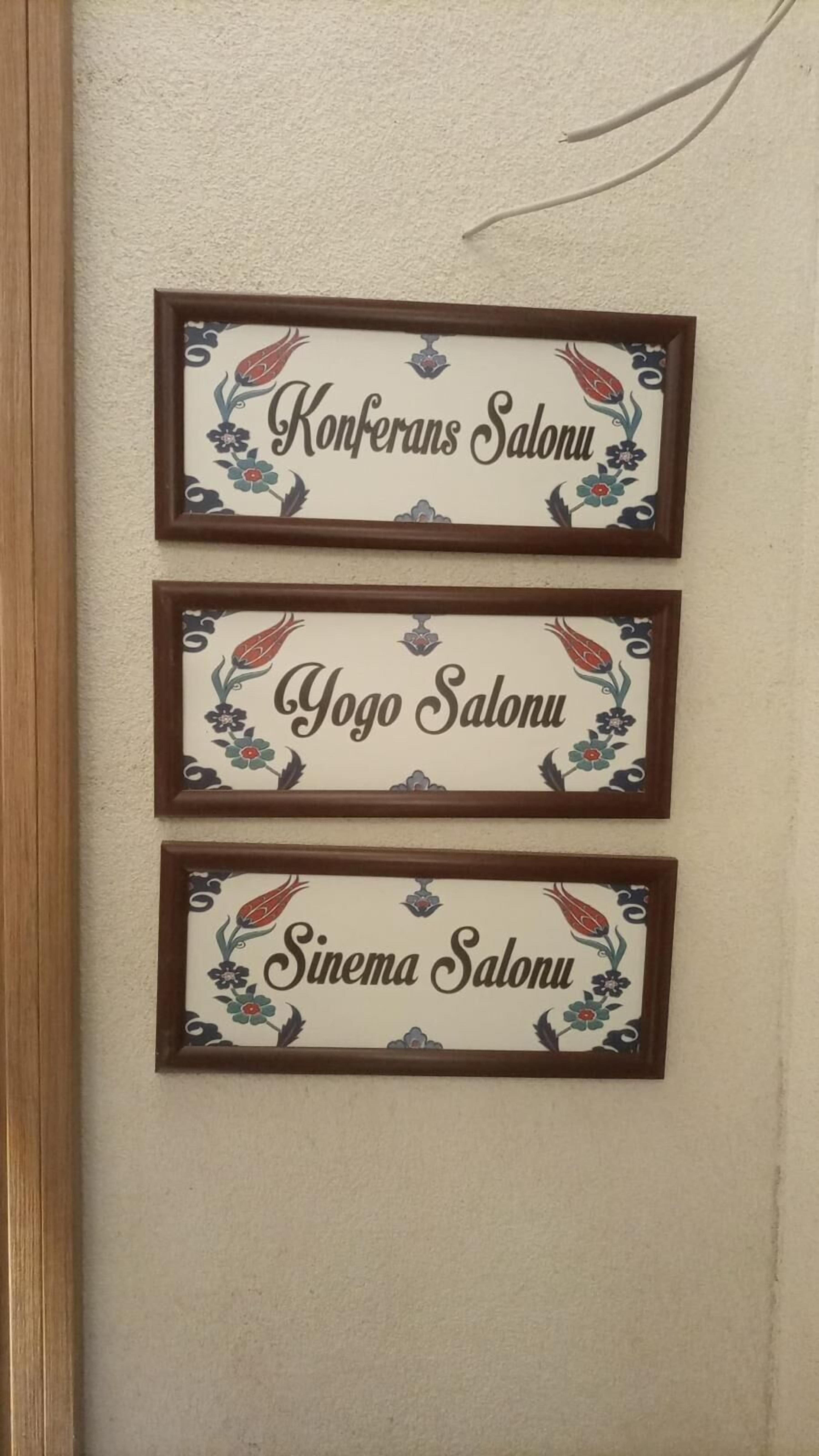 Three framed signs with floral designs and text indicating different salon names: Konferans Salonu, Yogo Salonu, and Sinema Salonu.