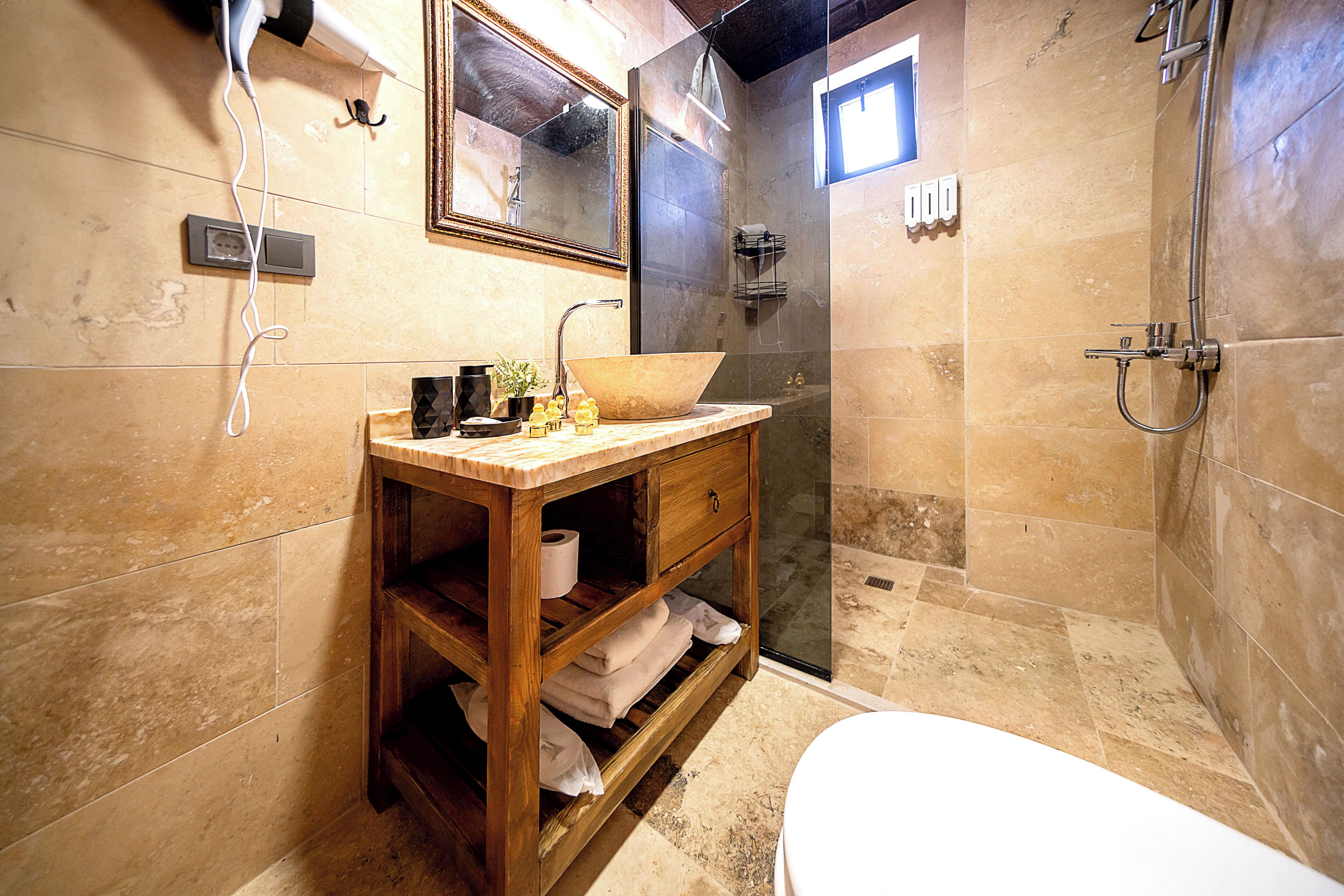 Een badkamer met een houten wastafelmeubel, een grote wasbak, een toilet en een douchehoek.