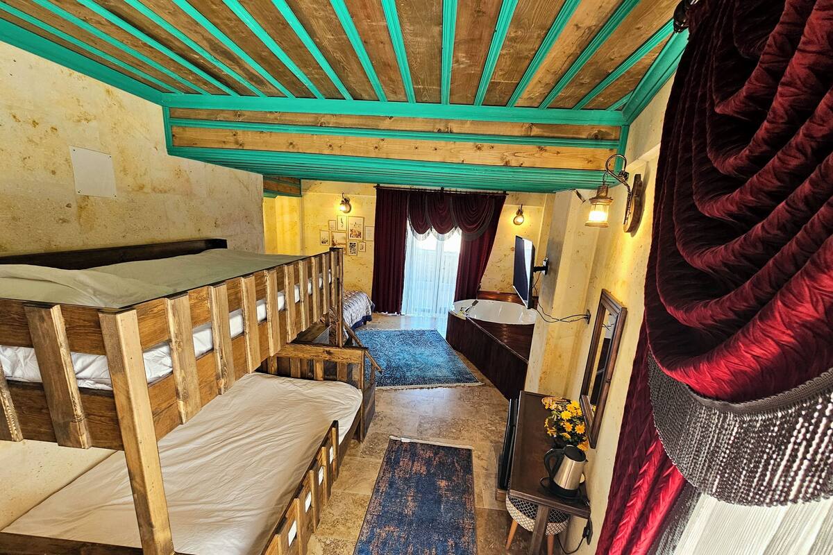 A rustic room with wooden bunk beds, a bathroom with a bathtub, and a small table with a flower vase.