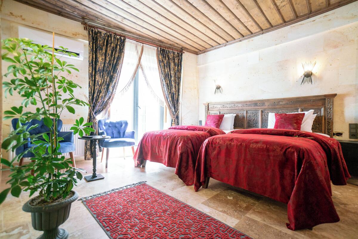 A room with two beds, a potted plant, a red rug, and a chair.