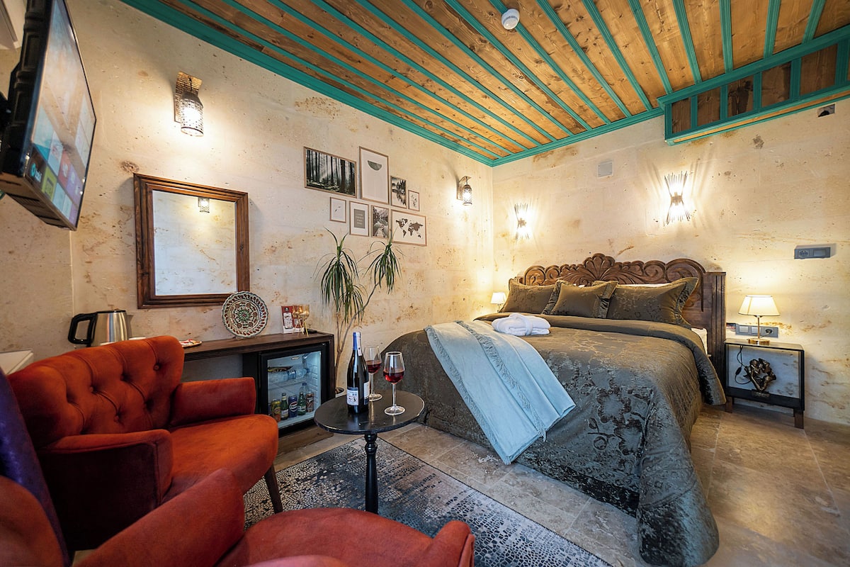 A cozy bedroom with a bed, a chair, a small table with a bottle and glass, and wall-mounted lights.