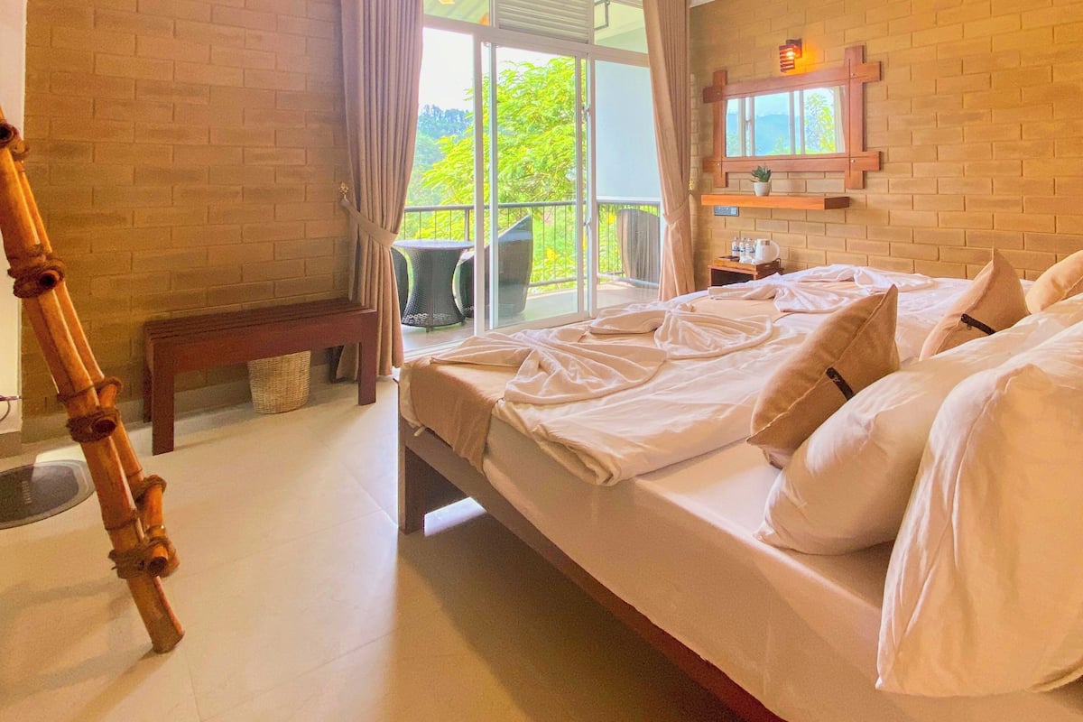 A bedroom with a bed, a bench, a window, and a view of greenery outside.