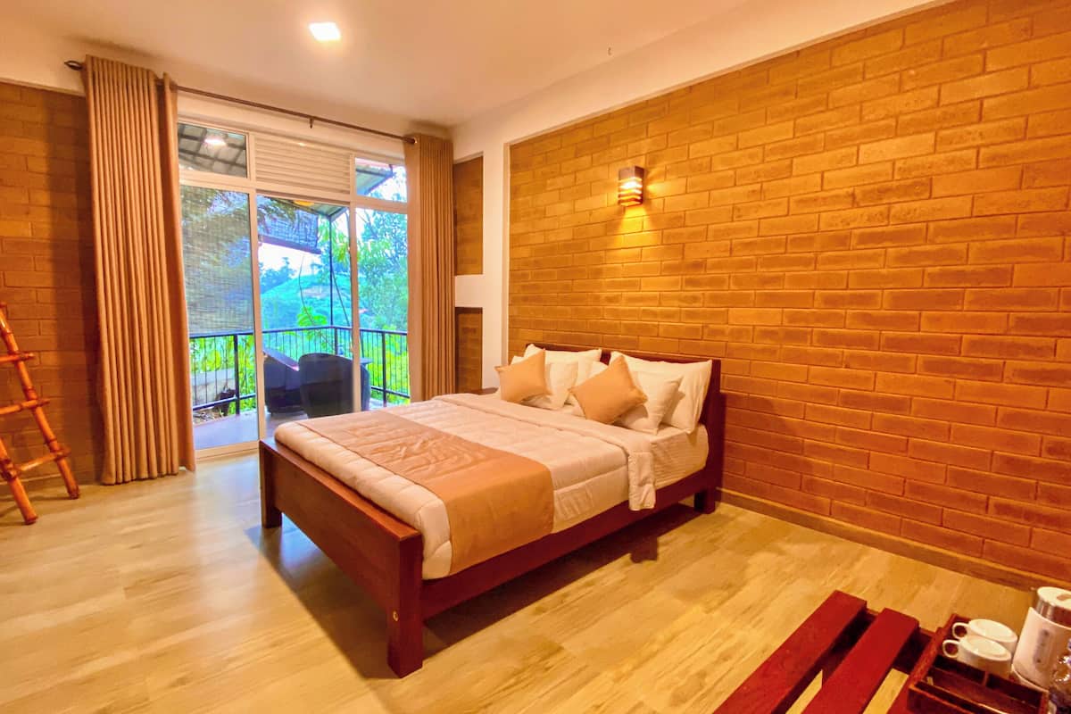 A bedroom with a wooden bed, a wooden floor, a balcony with a view, and a brick wall.