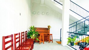 A spacious room with a long wooden bench along one wall, a wooden table with chairs, and a staircase with a metal railing leading to an upper level. - 90 Degrees Ella (Ella)