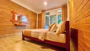 A bedroom with a wooden bed, a brick wall, a window with curtains, and a small shelf with a plant. - 90 Degrees Ella (Ella)