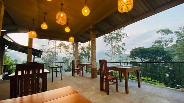 An outdoor seating area with tables and chairs, hanging lights, and a view of trees and hills. - 90 Degrees Ella (Ella)